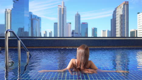 Rückansicht-Einer-Frau,-Die-Sich-Im-Luxuriösen-Dachpool-Mit-Atemberaubendem-Blick-Auf-Die-Wolkenkratzer-Von-Bangkok-Entspannt
