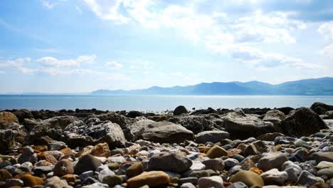 Colourful-variety-of-stone-boulders-beach-landscape-under-North-Wales-mountain-range-rise-jib-left-shot