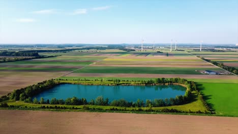 AERIAL---Lake-and-wind-energy-farm,-Deutsch-Brodersdorf,-Austria,-spinning-shot