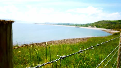 Barbed-wire-boundary-overlooking-calm-cliff-coast-countryside-waterfront-hiking-landscape-track-forward