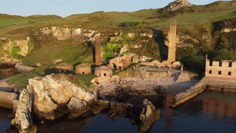 Porth-Wen-abandoned-coastal-derelict-brickworks-remains-golden-sunrise-countryside-bay-aerial-view-orbit-right