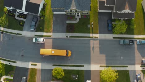 Top-down-aerial-of-yellow-school-bus-picking-up-students-in-housing-development-in-USA