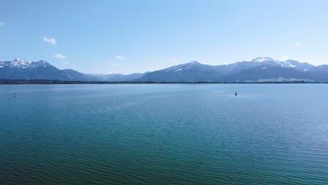 Vuelo-Panorámico-Bajo-Sobre-El-Lago-Chiemsee-Más-Famoso-De-Baviera-En-El-Campo-Rural-Con-Un-Hermoso-Cielo,-Agua-Azul-Clara-Y-Las-Impresionantes-Montañas-De-Los-Alpes-En-El-Fondo-En-Un-Día-Soleado
