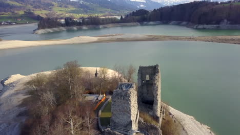 Aerial-forward-over-Gruyere-lake-with-ruins-Pont-en-Ogoz-castle-on-Oiseaux-island