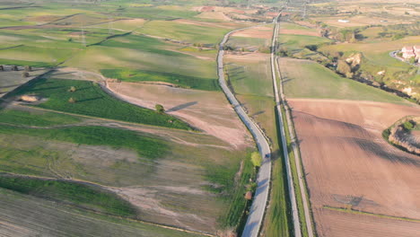 Aerial-Shot-of-a-Car-Driving-along-a-Road-Cutting-through-Agricultural-Farmland