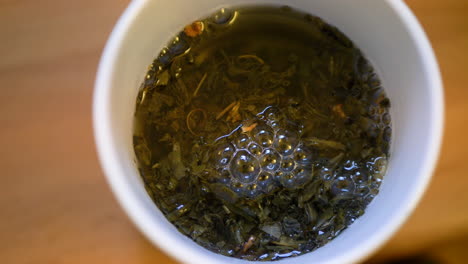 Close--up-From-The-Top-Of-Green-Cup-Of-Tea-In-Preparation-With-Steeping-Leaves