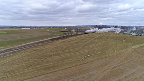 An-Aerial-View-of-an-Approaching-Steam-Train-Traveling-Thru-the-Countryside-Blowing-Smoke-and-Steam-on-a-Winter-Day