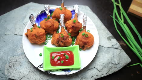 The-chef-served-the-well-cooked-crispy-chicken-lollipop-and-tomato-sauce-with-cutting-green-onion-on-it-in-a-plate