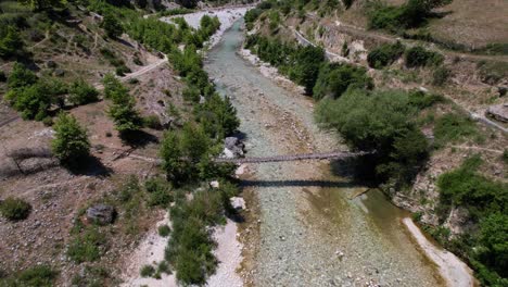 Wooden-hanged-bridge-on-banks-of-wild-river,-riverbed-on-valley-in-Albania