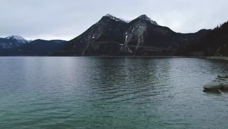 Szenische-4K-Niedrige-Luftaufnahme-Auf-Bayerns-Berühmten-Walchensee-Mit-Seinem-Besonderen-Blauen-Wasser-In-Der-Ländlichen-Bayerischen-Landschaft-Mit-Einem-Wunderschönen-Blauen-Himmel-Und-Den-Alpenbergen-Im-Hintergrund