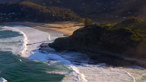 Schaumige-Wellen,-Die-In-Richtung-Küstenvorland-Mit-Cottages-Auf-Einem-üppigen-Plateau-Im-Royal-National-Park,-NSW,-Australien,-Rollen