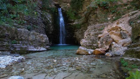 Waterfall-surrounded-by-rocky-slopes-of-canyon-and-pond-with-turquoise-clean-water-in-Albania