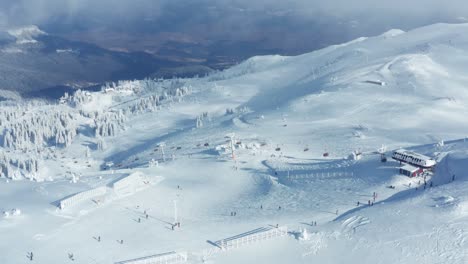 Atemberaubende-Schönheit-Des-Berges-Im-Winter-Und-Leute,-Die-An-Einem-Bewölkten-Tag-Auf-Der-Piste-Skifahren