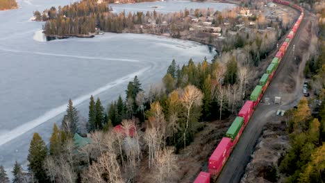 Aerial-follow-cam-of-a-colorful-freight-train-passing-by-small-group-of-cottages-in-the-Canadian-Shield