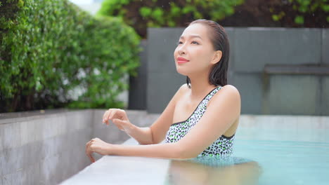 Close-up-of-a-young-woman-leaning-on-the-edge-of-an-infinity-edge-swimming-pool-checking-out-her-surroundings