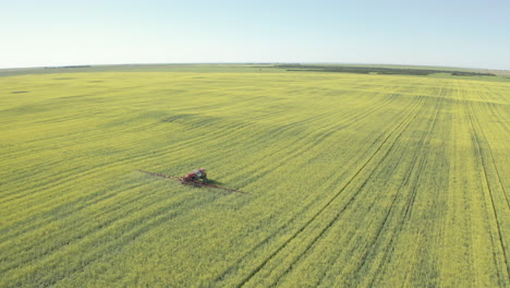Tractor-spraying-crops-in-green-sunny-field,-tracking-drone-shot