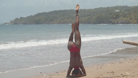 A-contortionist-in-a-hand-stand-position-before-dismounting-into-a-pose-with-waves-crashing-the-shoreline-in-the-background