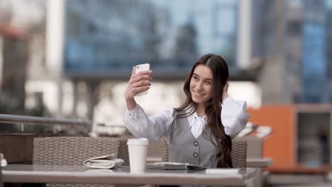 Stilvolle-Junge-Frau,-Die-Ein-Selfie-Am-Telefon-Macht,-Während-Sie-In-Einem-Café-Auf-Der-Straße-Sitzt