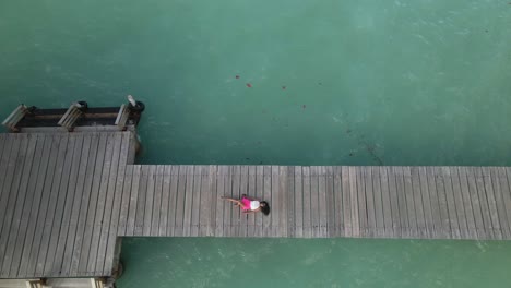 A-woman-in-a-pink-mini-skirt-laying-down-on-a-jetty-aerial-view-on-the-tropical-island-of-Tobago