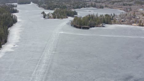 Aerial-circle-left-over-melting-frozen-lake-with-cracks-in-the-ice-roads-still-visible-in-Canada