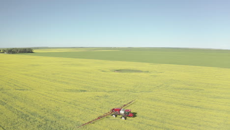 Two-Red-Farming-Tractor-Spraying-Fungicide-On-The-Flowering-Yellow-Canola-Field-In-Canada