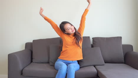 Asian-young-woman-in-casual-clothes-stretching-her-arms-over-the-head-while-sitting-on-a-sofa-daytime---static-shot
