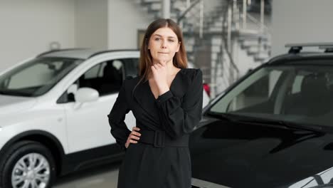 Beautiful-girl-in-a-black-dress-stands-on-a-background-of-cars-pondering-over-buying-a-car