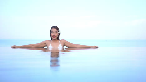 Asian-fit-Thai-woman-with-flower-in-her-hair-relaxing-inside-infinity-pool-front-view-daytime,-Hawaii-template-copy-space