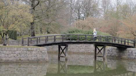 Girl-Wearing-Anime-Cosplay-Costume-Crossing-The-Wooden-Bridge-At-Japanese-Garden-In-Hasselt,-Belgium