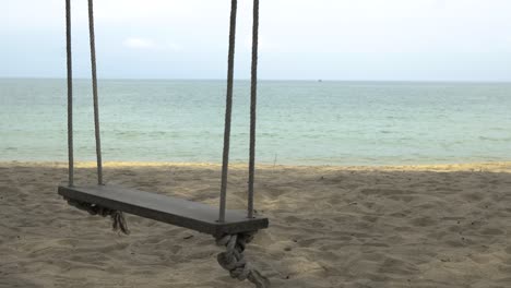 Close-up-one-wooden-swing-on-the-beach,-no-people,-blurred-background-of-sea-and-sky