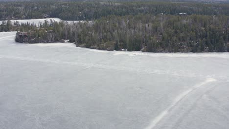 Aerial-dolly-left-over-melting-frozen-lake-with-cracks-in-the-ice-roads-still-visible-in-Canada