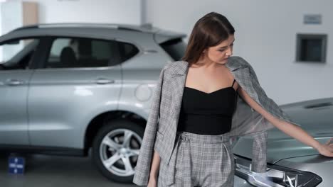 Stylish-fashionable-young-woman-posing-near-the-car-in-a-car-dealership