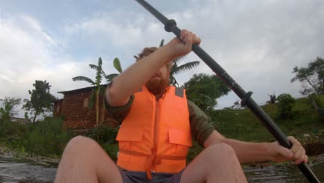 A-down-low-shot-of-a-bearded-man-in-a-life-jacket-paddling-from-the-shores-of-Lake-Victoria-in-rural-Africa