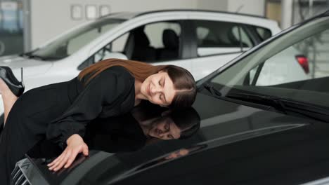 Beautiful-young-woman-in-a-black-dress-hugs-the-hood-of-a-new-car