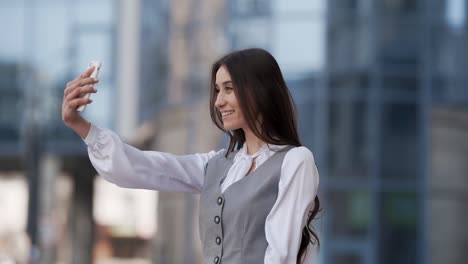 Cheerful-young-woman-in-a-business-suit-takes-a-selfie-video-on-a-smartphone