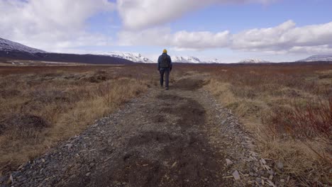 Backpacker-Walking-On-Stony-Trail-Through-Grassy-Field-Near-Bruarfoss-In-Brekkuskogur,-Iceland