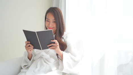 Sexy-beautiful-Asian-woman-in-bathrobe-relaxing-reading-book-in-hotel-room