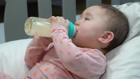 Little-infant-caucasian-baby-drinking-formula-milk-holding-bottle-by-herself-with-two-hands