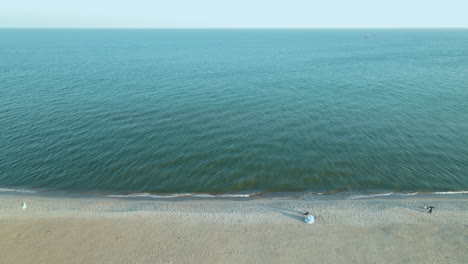 Aerial-tilt-down-shot-of-tourist-flying-kite-on-empty-beach-and-wide-Baltic-Sea-in-background