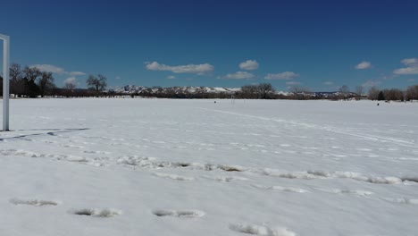 A-running-drone-shot-across-a-vacant-soccer-field-after-a-spring-snow