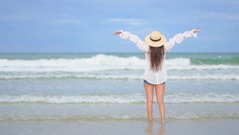 Back-view-of-woman-with-shorts-and-hat-on-seashore-raising-arms