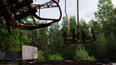 Rusty-amusement-park-swing-ride-in-Pripyat,-low-angle-zoom-out-view