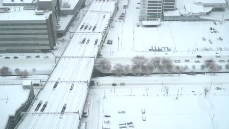 Looking-down-on-snowed-in-area-with-rail-tracks-and-cars-in-snowed-in-urban-area