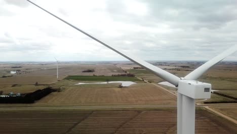 Aufsteigende-Luftaufnahme-Einer-Windkraftanlage-Und-Des-Ackerlandes-Und-Der-Teiche-Hinter-Den-Turbinenblättern