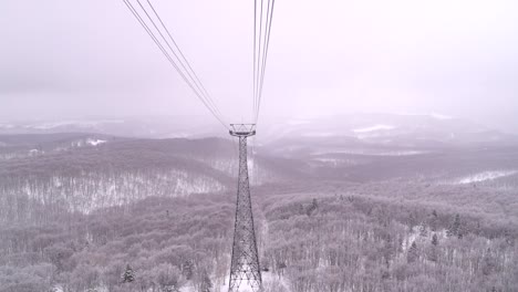 Slow-motion-view-from-front-of-cable-car,-riding-high-above-snowed-in-forest-in-nature-area