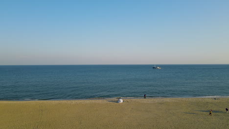 People-Leisurely-Walking-At-Seaside-Park-With-Fishing-Boat-Sailing-In-Blue-Ocean