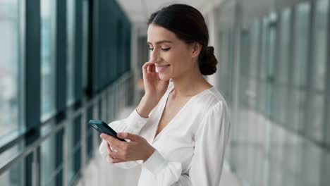 Pretty-young-business-woman-happily-meditating-with-a-smartphone-in-the-hallway