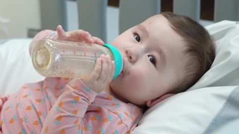Kleines-Kaukasisches-Babymädchen,-Das-Die-Letzten-Tropfen-Formelmilch-Trinkt-Und-Eine-Flasche-Mit-Zwei-Händen-Hält