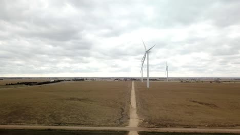 Langsame-Annäherung-Aus-Der-Luft-Entlang-Einer-Schotterstraße-Zu-Einer-Kleinen-Gruppe-Von-Windkraftanlagen-In-Einem-Winterfeld-Im-Ländlichen-Nebraska