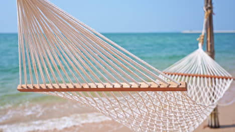 Empty-Hammock-on-Tropical-Beach-with-Blurry-Blue-Seascape-Background